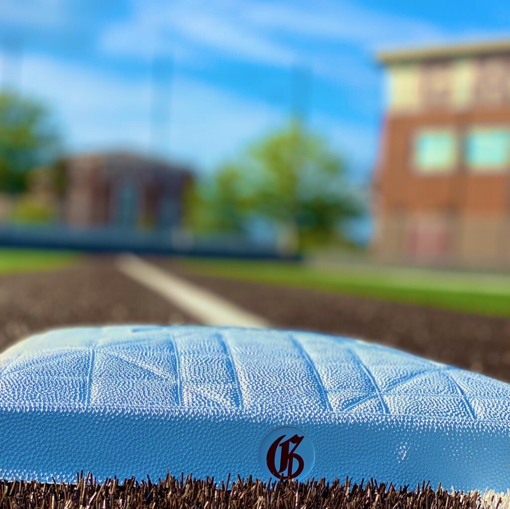 Close-up of a white base stamped with the G logo, the school building blurred behind it.
